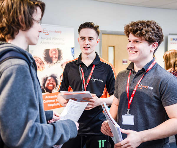 two young males wearing lanyards talking enthusiastically at an event to a third young male