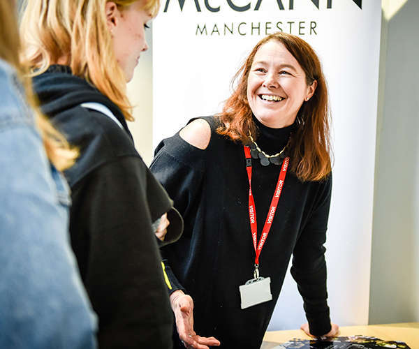 A woman wearing a visitor lanyard smiles at a group of young females