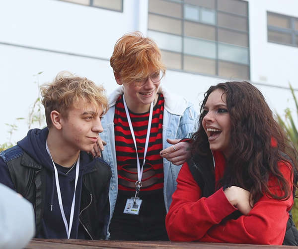 3 students, sat at a table outside laughing