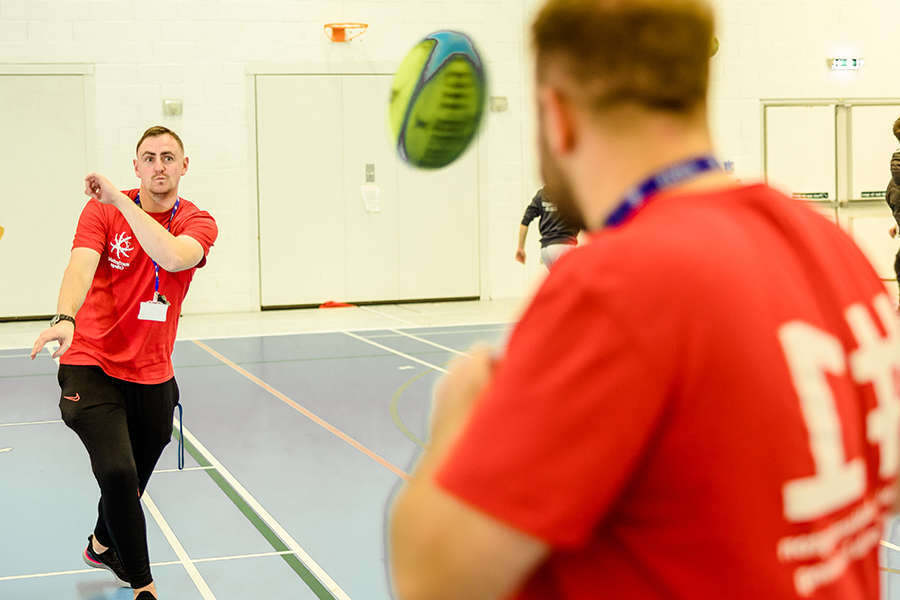 2 males practice throwing a rugby ball to each other